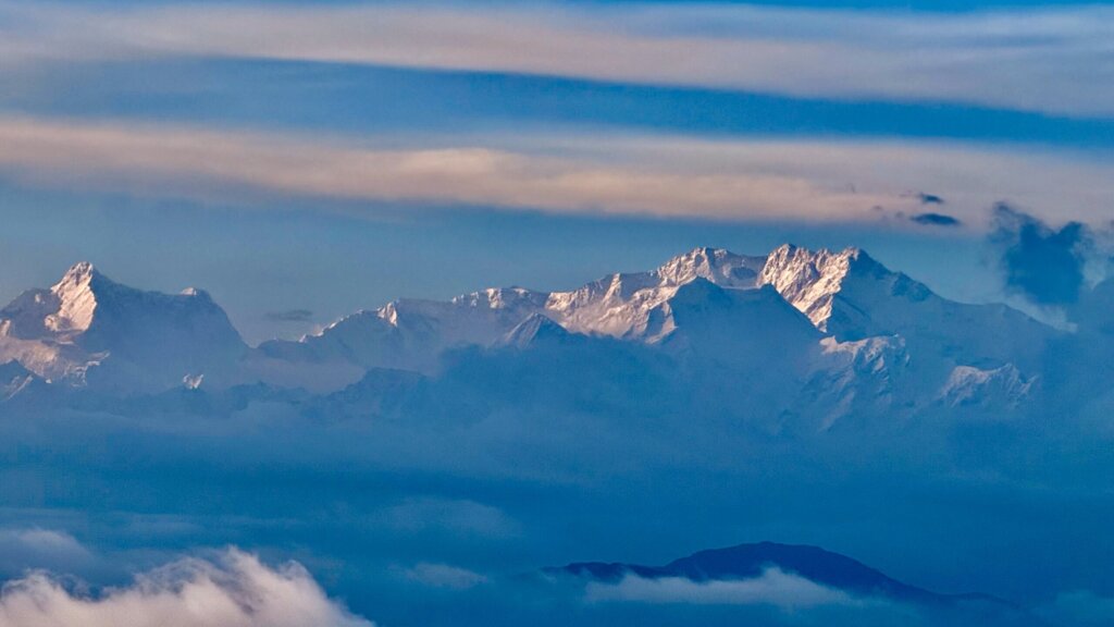 Majestätische, schneebedeckte Gipfel über einer Wolkendecke im Sonnenlicht.